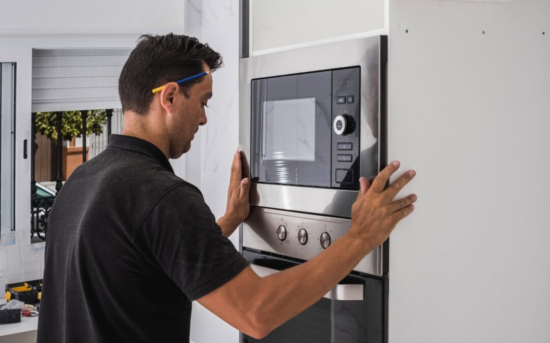 Man fitting a microwave inside the hole of a new kitchen cabinet